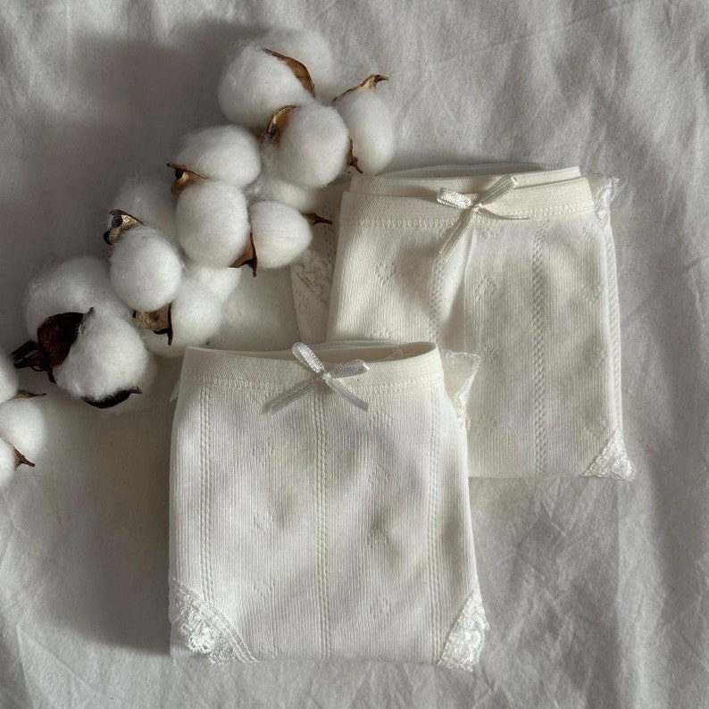 May include: Two pairs of white lace underwear with a delicate pattern. The underwear has a bow at the front and lace trim.