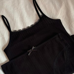 May include: Black lace-trimmed tank top and matching underwear. The tank top has thin straps and a ribbed texture. The underwear has a high-waisted fit.