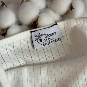 May include: White cotton fabric with a black label that reads "Sleepy but still pretty".