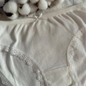 May include: White cotton underwear with delicate lace trim. The underwear has a ribbed texture and a bow detail at the front.