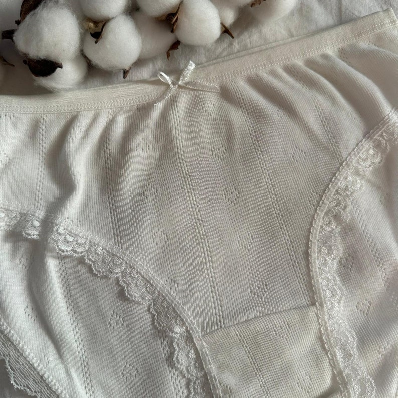 May include: White cotton underwear with delicate lace trim. The underwear has a ribbed texture and a bow detail at the front.