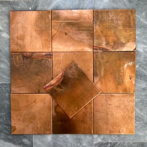 Puede incluir: Un conjunto de nueve azulejos de cobre dispuestos en un patrón cuadrado. Los azulejos tienen un aspecto rústico y envejecido con un tono cálido cobrizo.
