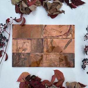May include: Six rectangular copper tiles with a rustic, aged finish. The tiles have a warm, reddish-brown colour with subtle variations in texture and shade.