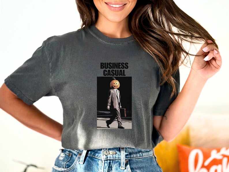 May include: Dark gray t-shirt with the words "BUSINESS CASUAL" above an illustration of a person with a pumpkin head wearing a suit and carrying a briefcase. The person is walking on a crosswalk.