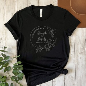 May include: Black t-shirt with a white floral design and the text "She is clothed with strength & dignity Proverbs 31:25"