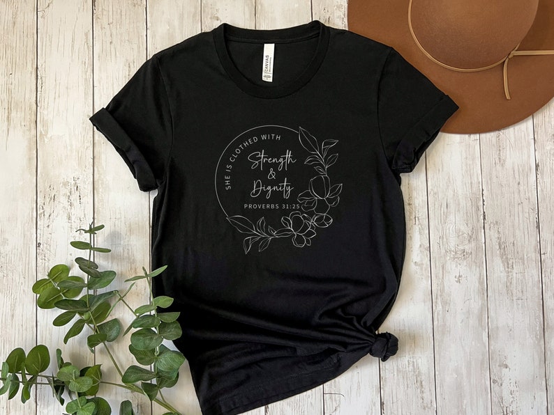 May include: Black t-shirt with a white floral design and the text "She is clothed with strength & dignity Proverbs 31:25"