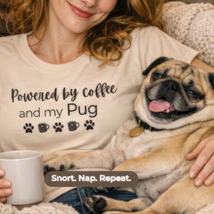 May include: A beige t-shirt with the text "Powered by coffee and my Pug" and paw prints and coffee cup graphics. A smiling pug dog is in the image. The text "Snort. Nap. Repeat." is at the bottom.