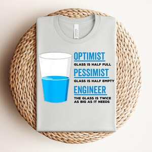 Puede incluir: Una camiseta gris claro con el texto "OPTIMISTA, EL VASO ESTÁ MEDIO LLENO, PESIMISTA, EL VASO ESTÁ MEDIO VACÍO, INGENIERO, EL VASO ES EL DOBLE DE GRANDE DE LO QUE NECESITA." Un gráfico de un vaso medio lleno de líquido azul está en la camiseta.