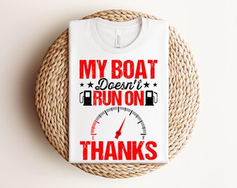 Puede incluir: Camiseta blanca con el texto rojo "MY BOAT Doesn't RUN ON THANKS" y un indicador de combustible. La camiseta está doblada sobre una superficie circular tejida.