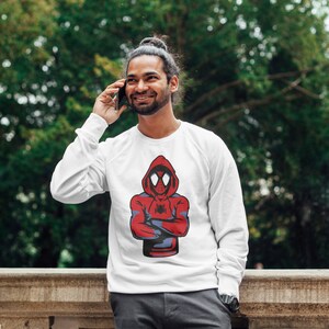 May include: White sweatshirt featuring a red and blue graphic of a hooded Spiderman character with a spider web on the chest.