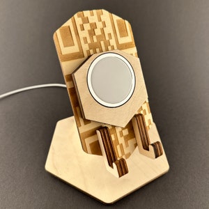 Könnte beinhalten: Holztelefonständer mit sechseckiger Basis und QR-Code-Design. Der Ständer hat einen runden Ausschnitt für ein kabelloses Ladegerät.