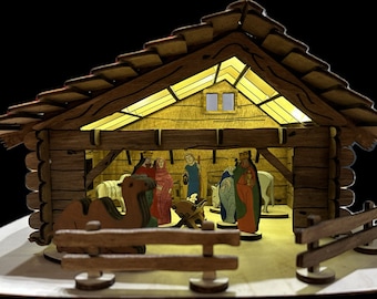 Op de afbeelding: Een houten kerststal met een bruin dak, een verlicht interieur en figuren van Maria, Jozef, baby Jezus en de drie wijzen uit het oosten. De scène speelt zich af in een stal met een kameel en een ezel.