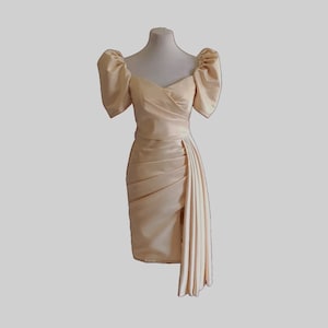May include: A cream satin dress with a fitted bodice and a flowing skirt. The dress has a V-neckline and puffed sleeves.