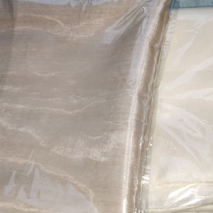 Może przedstawiać: Dwa rolki przezroczystej tkaniny, jedna beżowa, a druga biała, zapakowane w plastik.