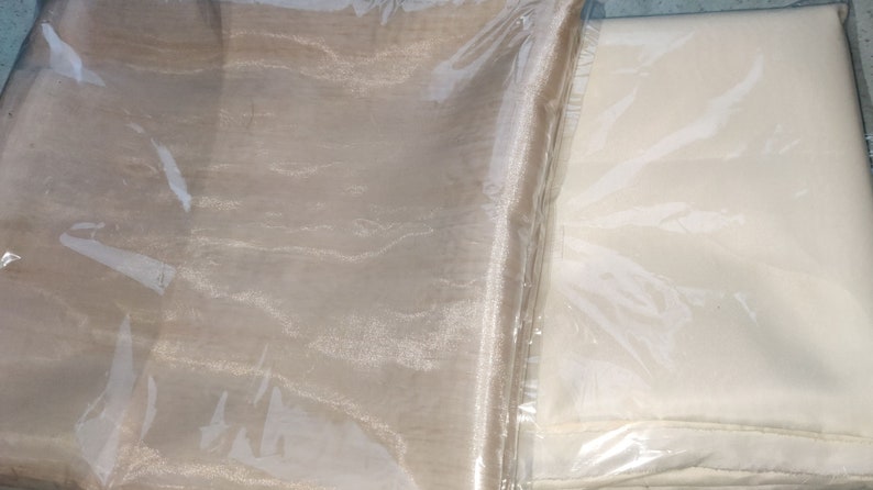 Może przedstawiać: Dwa rolki przezroczystej tkaniny, jedna beżowa, a druga biała, zapakowane w plastik.
