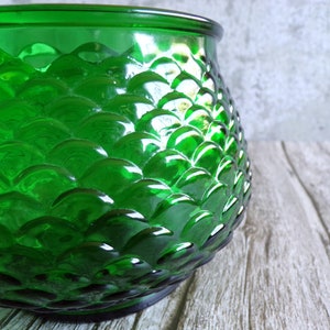 May include: A vibrant green glass jar with a textured, scale-like pattern. The jar has a rounded shape and a smooth rim. The glass reflects light, creating highlights and shadows. The jar is likely used for storage or decoration.
