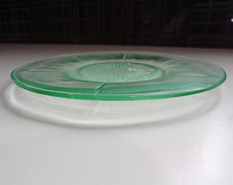May include: A green glass plate with a scalloped edge and a raised, starburst pattern in the center.