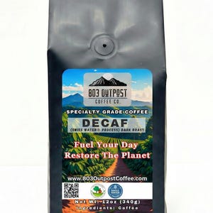 May include: A black bag of decaf coffee from 803 Outpost Coffee Co. The label features a mountain scene and the words "Fuel Your Day, Restore The Planet." The bag contains 12 oz (340g) of coffee.