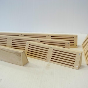 May include: Five wooden vent covers with a slatted design. The covers are arranged in a staggered pattern on a light wood surface.