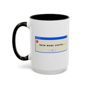 May include: White coffee mug with a black handle and interior. The mug features a "Fatal Error" message box with the text "NEED MORE COFFEE...." and an "OK" button, ideal for coffee drinkers.