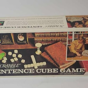 May include: A box for the Scrabble Sentence Cube Game. The box is white with a red, white and blue colour scheme. The box features a picture of a couple playing the game. The box also features the Scrabble logo and the words "Sentence Cube Game".