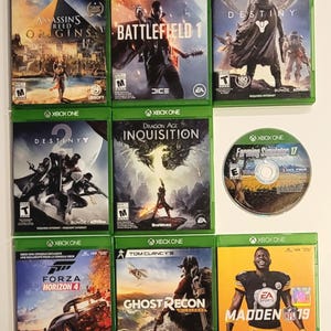 May include: A collection of ten Xbox One video game cases, featuring titles such as Assassin's Creed Origins, Battlefield 1, Destiny, Dragon Age: Inquisition, Forza Horizon 4, Ghost Recon Wildlands, and Madden NFL 19. The cases are arranged in two rows of five, with the game titles and logos clearly visible.