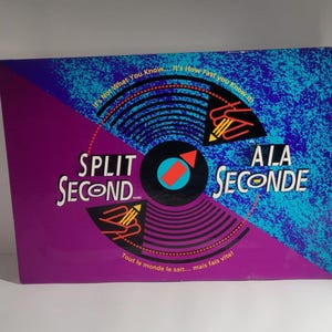May include: A purple and blue game box with a black and white record design. The game is called "Split Second" and "Ala Seconde". The text on the box reads "It's not what you know... It's how fast you know it!" and "Tout le monde le sait... mais fais vite!"