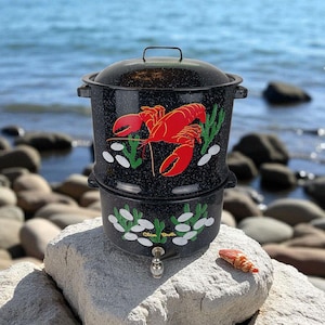 Puede incluir: Olla de langosta de esmalte negro con un diseño de langosta roja, algas verdes y conchas blancas. La olla tiene tapa y grifo. Las palabras "Clam Broth" están impresas en la sección inferior. Una pinza de langosta descansa sobre una roca.