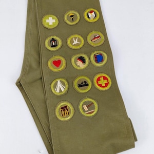 May include: Olive green sash with embroidered patches. Patches include a white cross, a torch, a book, a lantern, a bird, a shoe, a heart, a Native American profile, a book, a tent, a saw, a red cross, a chair, and a hammer.