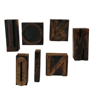 May include: A collection of seven vintage wooden letterpress blocks featuring various characters including the letters I, O, K, M, N, and a thin vertical bar. Each block has a dark, weathered brown finish with visible signs of age and wear.