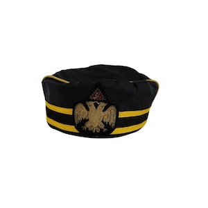 Puede incluir: Sombrero negro con ribete dorado y dos rayas amarillas. Presenta un águila dorada bordada y un símbolo de triángulo rojo. Este sombrero es probablemente para uso ceremonial o fraternal.
