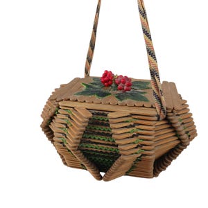 Puede incluir: Un bolso único, hecho a mano, construido con palitos de helado de madera. El bolso presenta un diseño geométrico con detalles verdes y una parte superior decorativa con bayas rojas y hojas verdes. Tiene una correa estampada.