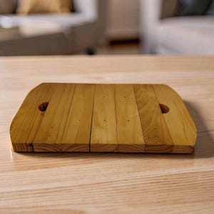 May include: A rectangular wooden serving board constructed from five parallel light brown pine planks. The board features rounded corners and two circular cut-out handles, one on each side, with visible wood grain and small dark knots.