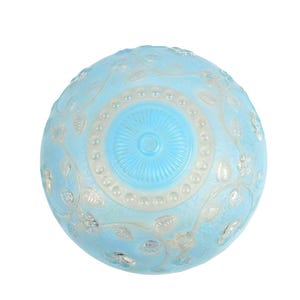 May include: A round, light blue glass lamp shade featuring a raised, frosted white floral and vine pattern. The center of the shade displays a circular, sunburst-style design surrounded by a ring of small, raised, translucent glass beads.