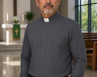 May include: A long-sleeved charcoal gray clergy shirt featuring a mandarin collar with a white tab insert and a single chest pocket. The shirt is buttoned down the front and is paired with black trousers held by a black leather belt with a silver buckle.