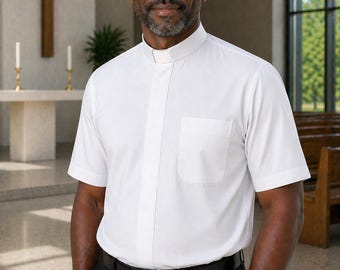 May include: A short-sleeved white clergy shirt featuring a traditional tab collar insert, a concealed button placket, and a single chest pocket. The shirt is worn tucked into black trousers secured with a simple black leather belt with a silver buckle.