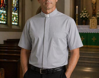 May include: A light gray short-sleeved clergy shirt featuring a white clerical collar insert, a front button placket, and a single chest pocket, paired with black trousers and a black leather belt with a silver-toned metal buckle.