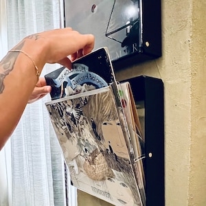 Può includere: Un'unità di archiviazione per dischi neri con un inserto in plastica trasparente. L'inserto contiene una pila di dischi in vinile con copertine di album che mostrano il testo "The Moody Blues", "Question of Balance" e "Revolver".