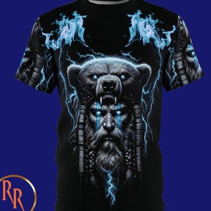 以下が含まれることがあります： 黒いTシャツ。青い稲妻と炎を伴い、あごひげを生やした顔の上にクマが描かれた印象的なグラフィック。このデザインは、複雑なディテールと大胆なカラーパレットを備え、視覚的に印象的な美しさを生み出しています。