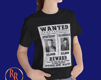 Può includere: Maglietta nera con un design di poster vintage ricercato con immagini di Butch Cassidy e il Sundance Kid. Il poster offre una ricompensa di $ 5.000 per la loro cattura, vivi o morti.