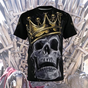 以下が含まれることがあります： 金色の王冠をかぶった、詳細なスカルが特徴の黒いTシャツ。スカルはグレーと白の色合いで表現され、王冠はメタリックゴールドです。デザインはシャツの中央に配置され、大胆な印象を与えます。
