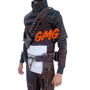 May include: Brown and white costume with a high collar, shoulder strap, and multiple pouches. The costume includes a belt, pants, and a holster. The text "GMG" is visible on the chest. The outfit has white stitching.
