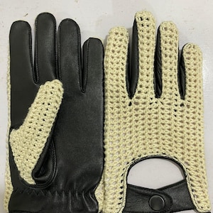 May include: A pair of black leather driving gloves with a cream-coloured crocheted back. The gloves have a button closure at the wrist and a vent on the palm. The gloves are designed for driving and offer a stylish look.