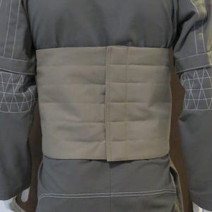 Puede incluir: Chaqueta gris con cintur&oacute;n acolchado beige. La chaqueta tiene detalles de costura blancos en las mangas y los bordes. El cintur&oacute;n es rectangular y acolchado, con costuras horizontales.