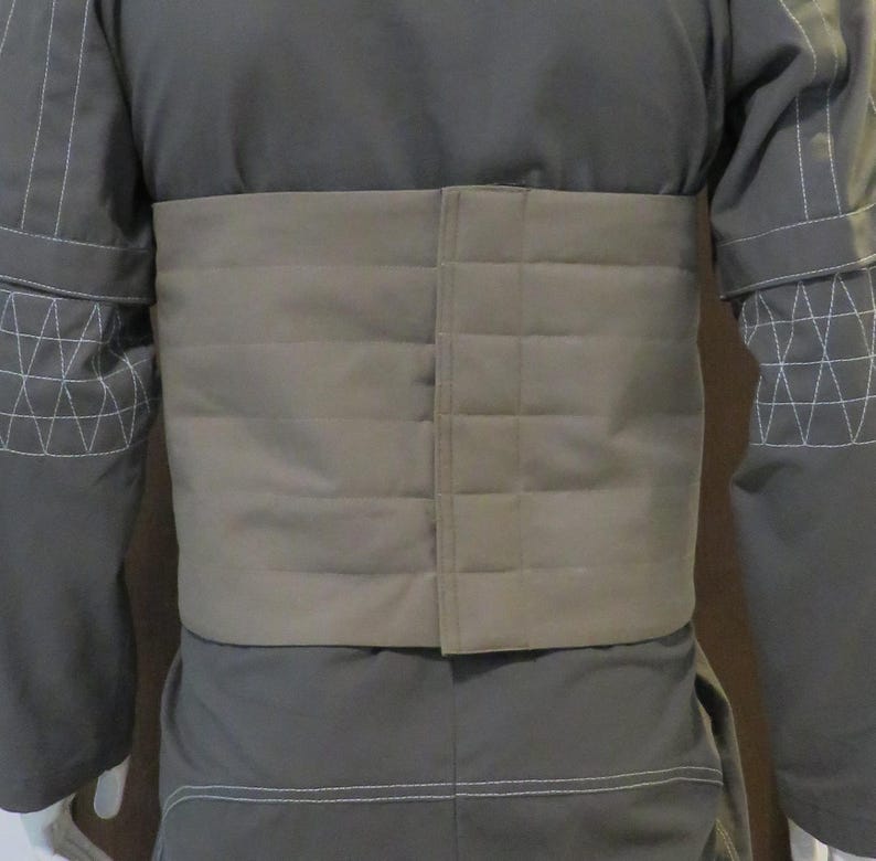 Puede incluir: Chaqueta gris con cintur&oacute;n acolchado beige. La chaqueta tiene detalles de costura blancos en las mangas y los bordes. El cintur&oacute;n es rectangular y acolchado, con costuras horizontales.