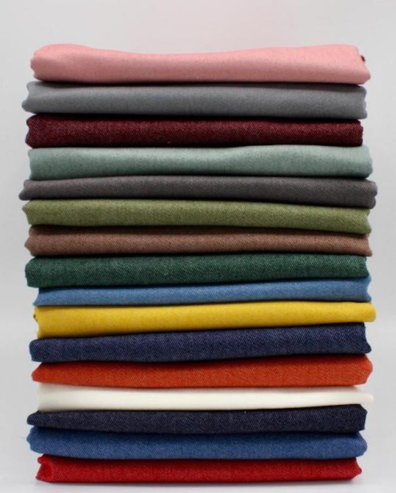 May include: A stack of folded fabric in various colors, including pink, gray, burgundy, green, yellow, and navy blue. The fabrics are neatly arranged, showcasing a range of hues suitable for sewing or crafting projects. The image is well-lit, highlighting the textures and colors.