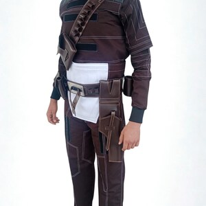 May include: Brown and black costume with white stitching, featuring a high collar, multiple pockets, and a belt with pouches. The outfit includes a shoulder strap with additional storage and is designed for a unique look.