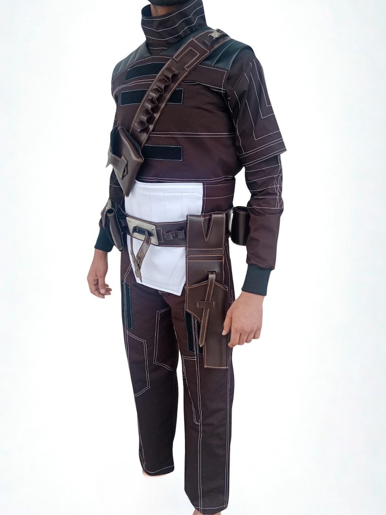 May include: Brown and black costume with white stitching, featuring a high collar, multiple pockets, and a belt with pouches. The outfit includes a shoulder strap with additional storage and is designed for a unique look.