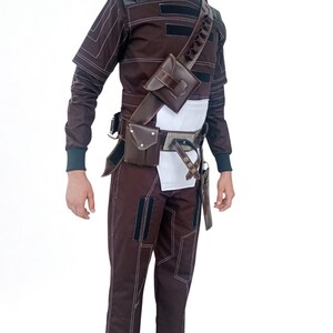 May include: A brown and black costume with white stitching, featuring a high collar, long sleeves, and matching pants. The outfit includes a leather shoulder strap with pouches, a belt with additional pouches, and a white midsection.
