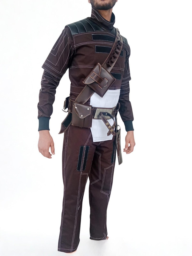 May include: A brown and black costume with white stitching, featuring a high collar, long sleeves, and matching pants. The outfit includes a leather shoulder strap with pouches, a belt with additional pouches, and a white midsection.